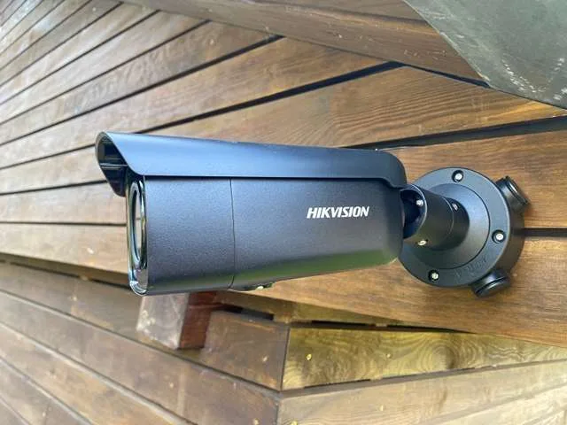 Tmavá kamera Hikvision na dřevěném obkladu domu