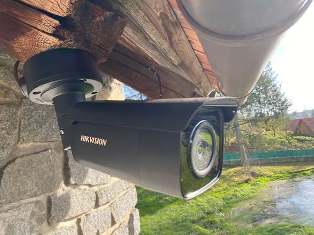 Černá kamera Hikvision pod okapem u kamenné zdi